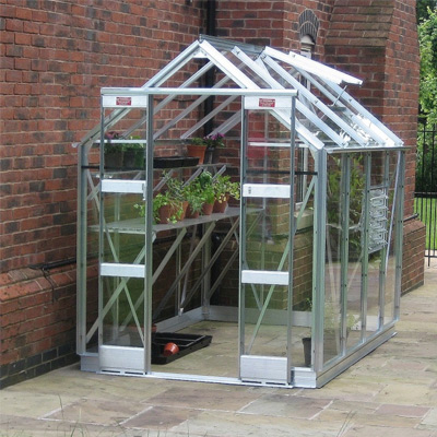 small aluminium greenhouse in silver next to brick wall