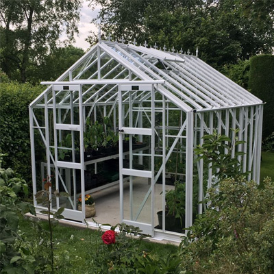 white victorian style aluminium greenhouse in garden