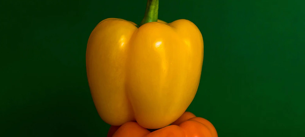 yellow pepper placed on top of an orange pepper
